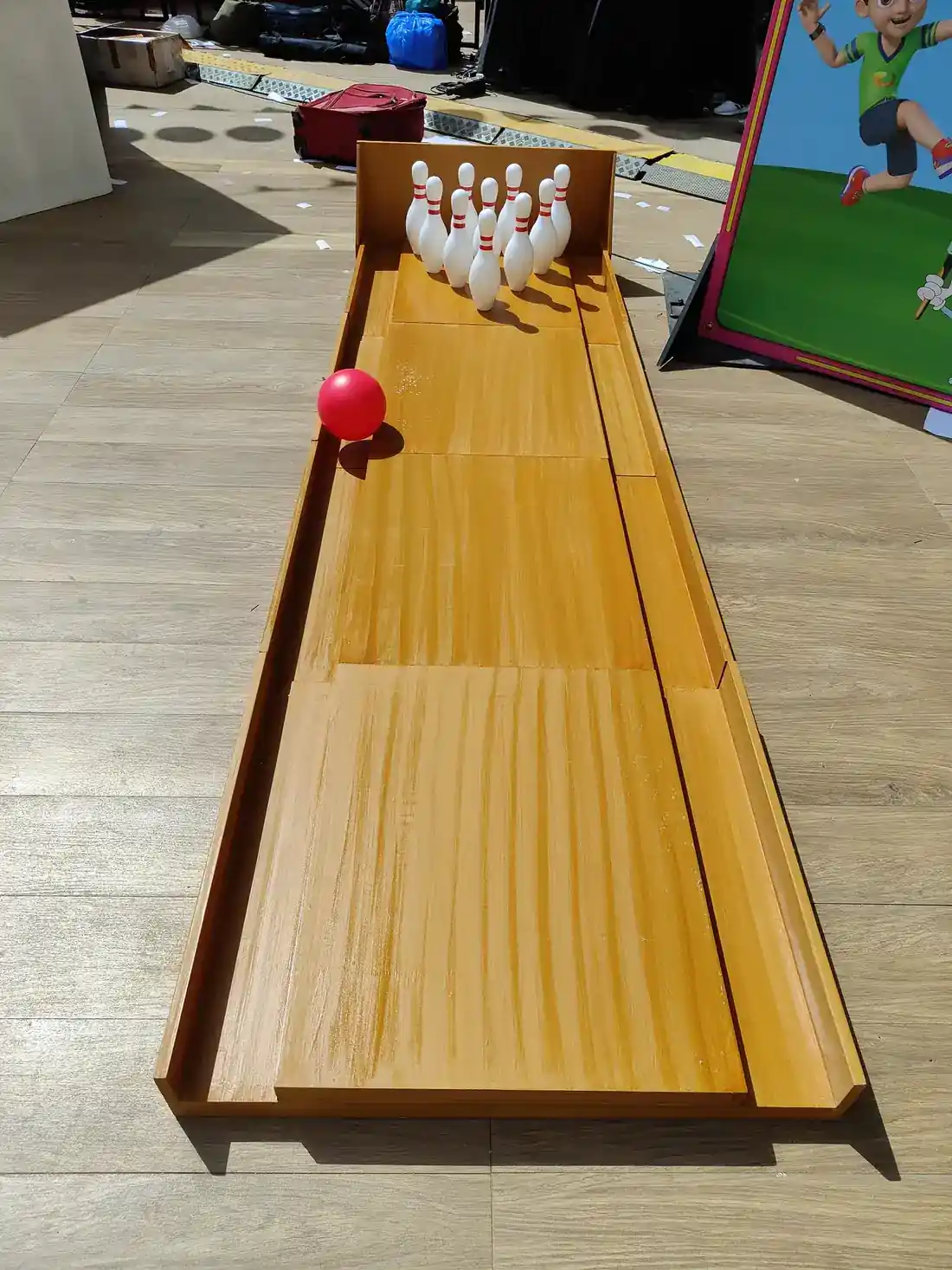 Wooden portable bowling alley with white pins and red ball